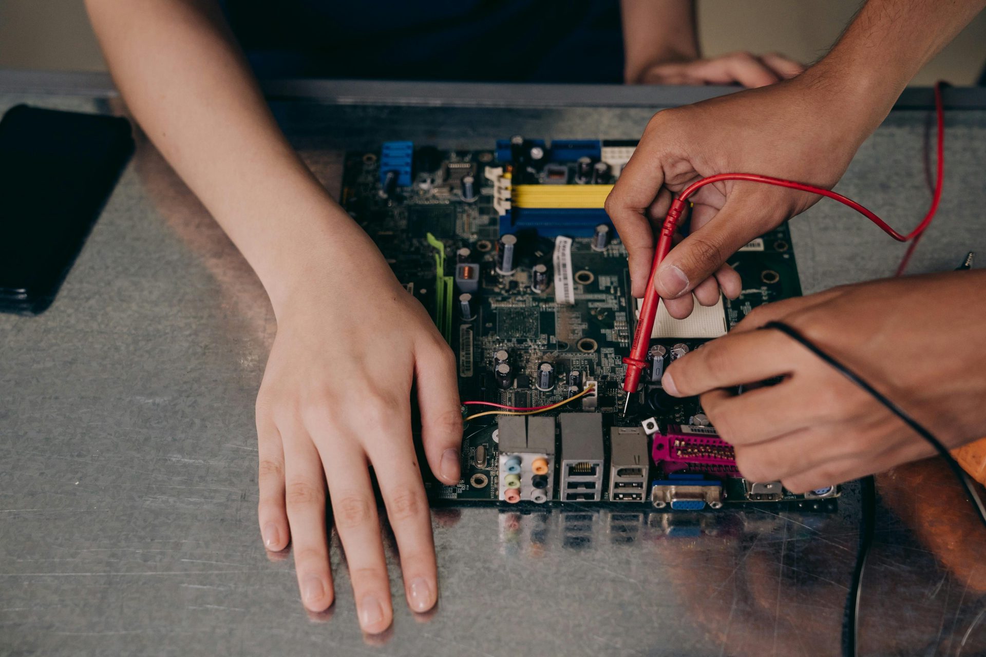 Hands working with electrical tester on motherboard, showcasing technical repair skills.